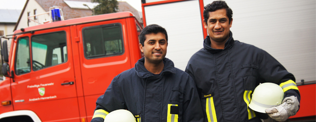 Zwei Feuerwehrmänner mit Migrationshintergrund vor einem Feuerwehrauto